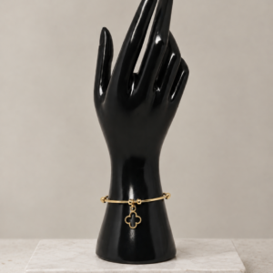 Gold-tone stainless steel bangle bracelet with open clover charm, on a black hand display