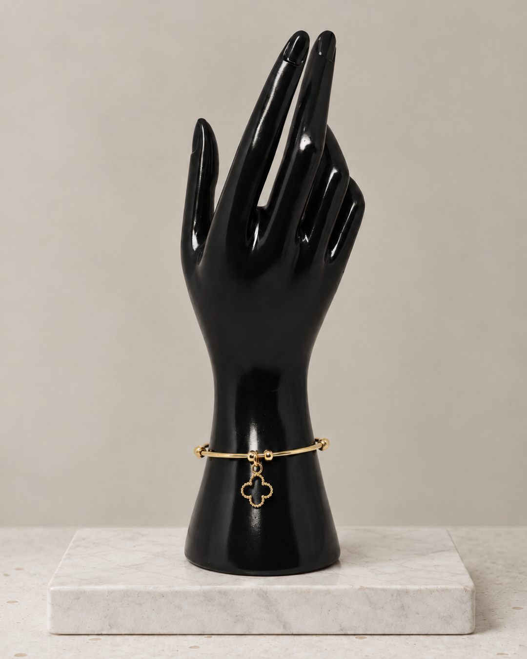 Gold-tone stainless steel bangle bracelet with open clover charm, on a black hand display